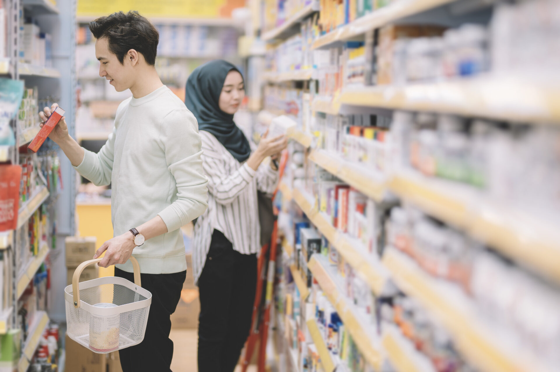 asian chinese and malay customers shopping, selecting, choosing and buying at the pharmacy store in the aisle with shopping basket
